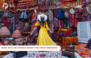 Merry Morocco tour card for Three Days Erg Chebbi Desert Tour from Marrakech showing a woman in yellow caftan at colorful souk market