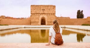 Female tourist with leather backpack sitting at El Badi Palace reflecting pool in Marrakech