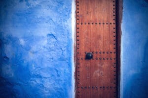 Close-up of traditional wooden studded door set in a brilliant blue plastered wall in Chefchaouen Morocco