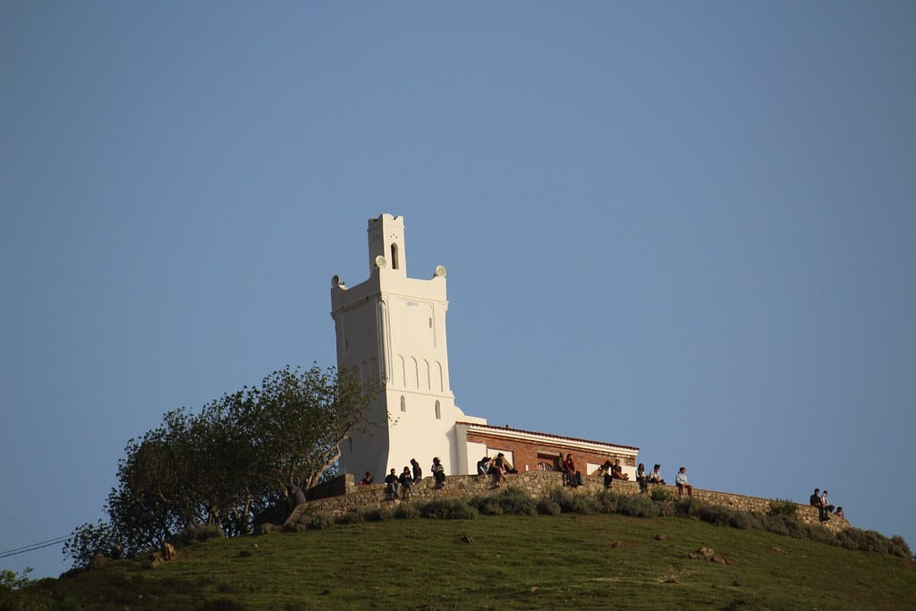White Spanish Mosque minaret on a green hill above Chefchaouen with visitors gathered